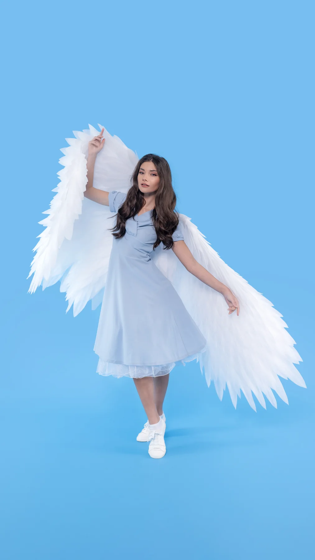 Model wearing white angel wings against a blue backdrop